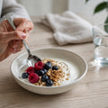 Kleine Mahlzeit mit Joghurt, Beeren, Haferflocken und Walnüssen auf einem hellen Tisch.